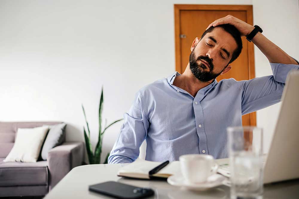 Person-struggling-with-msk-pain - optima health Person struggling with neck pain while working at a desk